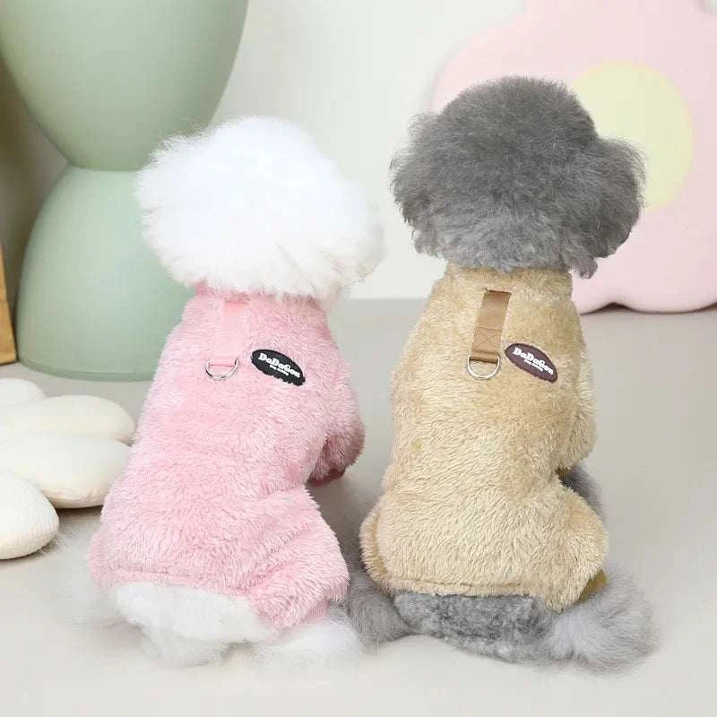 Two small dogs wearing soft fleece elastic pet jumpsuits with pull rings, one in pink and one in beige, sitting indoors