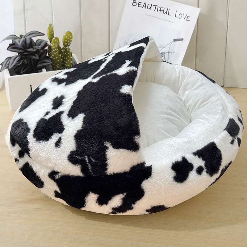 Plush pet cat bed with black and white cow print, ultra-soft plush fabric, deep cozy round design, and non-slip bottom for stability.