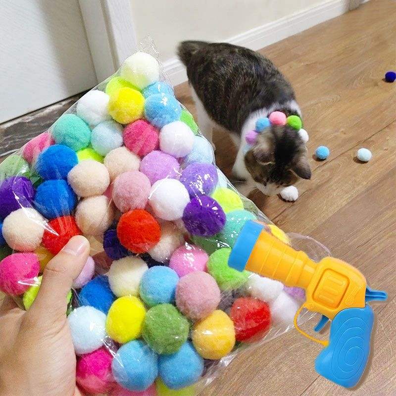 Colorful pom-pom balls with a toy launcher and a cat wearing pom-poms, not an automatic ball launcher for dogs