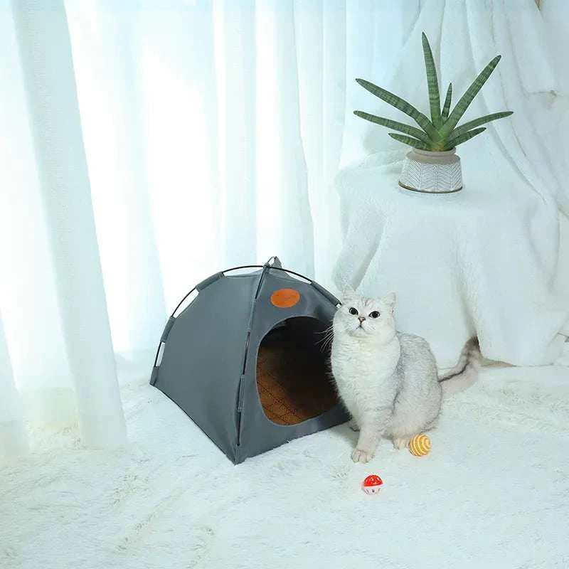 Foldable pet tent with gray fabric and mesh windows, shown with a white cat sitting nearby on a white floor in a bright room.